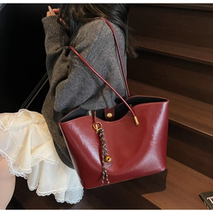 Close-up of wine red glossy leather tote bag with gold hardware and charm on wooden steps