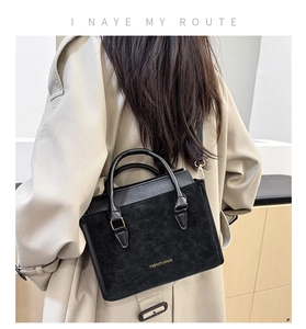 Dettaglio di una borsa a tracolla nera con texture scamosciata e logo dorato raffinato
