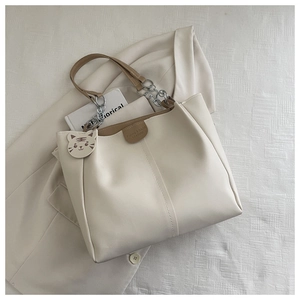 Detail of cream tote bag featuring brown leather handles and a tiger charm on suit