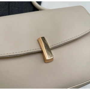 Detailed close-up of beige leather bag featuring a minimalist gold rectangular clasp