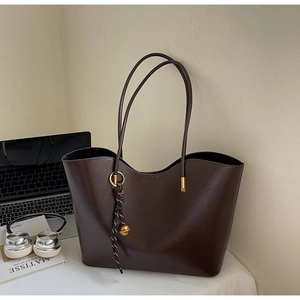 Deep brown matte leather tote bag with unique curved top edge and hanging charm detail