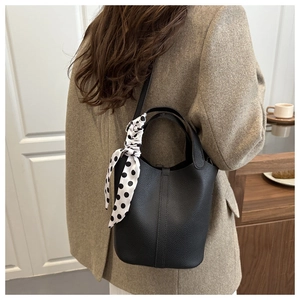 Detail of black pebbled leather bucket bag with a stylish polka dot scarf on the handle