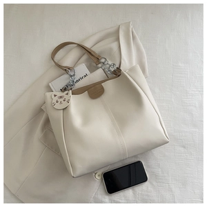 Detail view of off-white tote bag with silver chain strap and tiger charm on white blazer