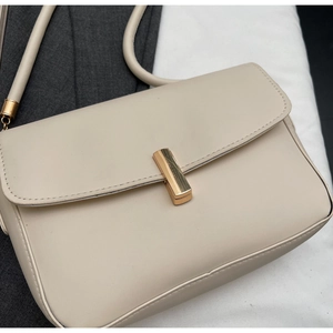 Close-up of elegant cream leather crossbody bag with modern gold rectangular metal clasp