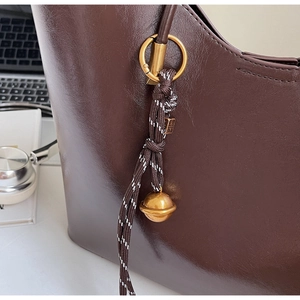 Macro shot of dark brown glossy leather tote bag with elegant metallic charm details