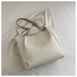 Minimalist cream tote bag with brown handles and silver chain detail on office suit
