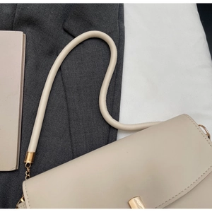 Close-up of beige leather handbag with gold clasp and tubular strap on a grey suit
