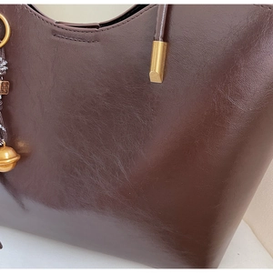 Detailed macro of glossy brown leather handbag with golden metal hardware and charms