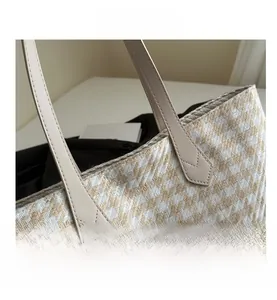 Close-up of herringbone woven tote bag with beige leather handles and reinforced stitching