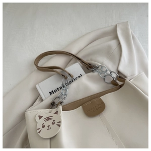 Detail of beige tote bag featuring silver chain straps and a cute tiger charm accessory