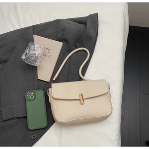Detail of cream faux leather shoulder bag with gold clasp on white bedding and grey blazer