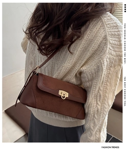 Detail of brown leather and suede shoulder bag with gold metal buckle on a beige sweater
