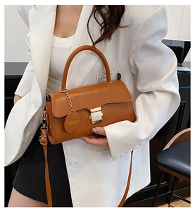 Détail d'un sac bandoulière en cuir marron avec boucle en métal et étiquette ronde