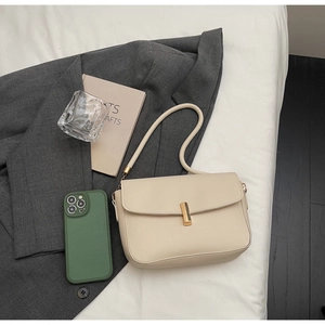 Detail of elegant cream shoulder bag featuring a sleek gold metal bar clasp and leather strap