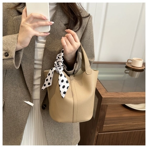 Detail of cream leather bucket bag featuring a polka dot silk scarf tied on the handle