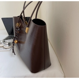 Detail view of coffee brown leather tote bag with elegant decorative tassel and long strap