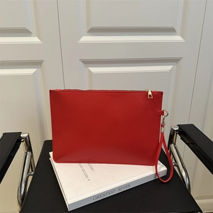 Elegante pochette a busta rossa con cerniera dorata e cinturino su sfondo di un libro