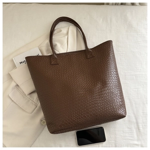 Detail shot of a dark brown large tote bag with woven texture on a white fabric surface