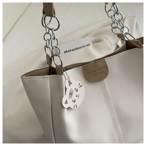 Close-up of leather tote bag featuring metal chain strap and cute tiger head charm accessory
