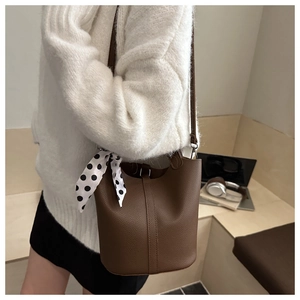 Détail d'un sac seau en cuir marron foncé avec une écharpe en soie à pois sur la poignée