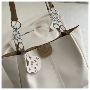 Detail of cream tote bag with brown trim, silver chain strap and tiger charm