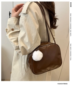 Detail of dark brown glossy patent leather shoulder bag with white fluffy charm