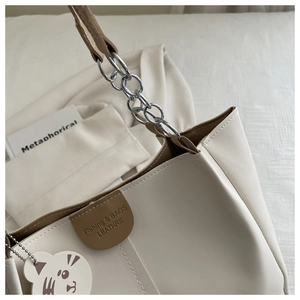 Close-up of cream tote bag with silver chain strap and cute cat charm detail