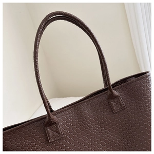 Detailed close-up of dark brown woven leather texture and handle joint on a tote bag