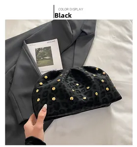 Dettaglio di pochette nera leopardata con borchie dorate su sfondo di giacca grigia