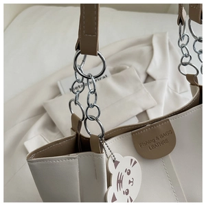 Detail of color-block tote bag featuring silver chain handle and cartoon tiger charm