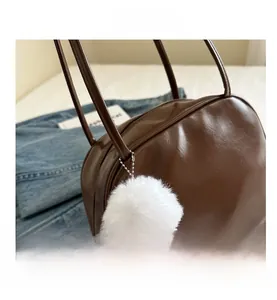 Detail of dark brown leather handbag with round lines and white plush ball charm accessory