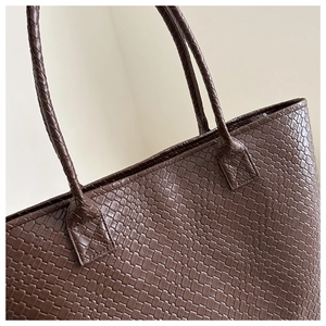 Detail of reinforced X-shaped stitching on dark brown woven texture tote bag