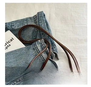 Detail view of the brown leather shoulder bag handle and stitching on white fabric