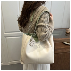 Detail of tote bag showing green leather strap stitching and cute cat charm attachment