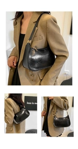 Detail of black glossy crackle leather baguette bag showing texture and crescent silhouette