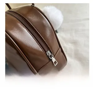 Detailed macro view of smooth metal zipper and white plush ball on dark brown leather bag