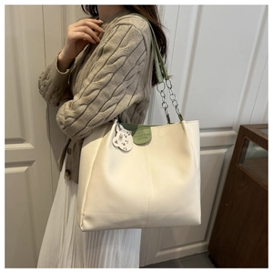 Detail view of large tote bag featuring green leather accents and cute cat pendant