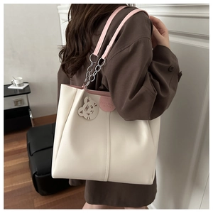 Detail of cream tote bag with pink straps, chain metal hardware, and cute cat charm