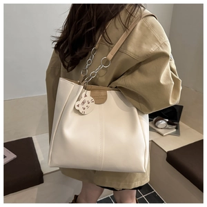 Detail of cream white tote bag featuring brown leather strap and cute cat charm accessory