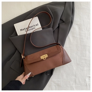 Detail of a brown leather baguette bag with a vintage gold buckle on a grey blazer and book
