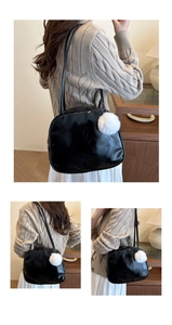 Detail of black glossy shoulder bag with white pom-pom charm and dual slim straps
