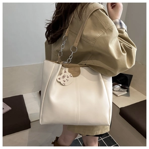Detail of minimalist cream tote bag featuring brown leather trim and cute tiger charm