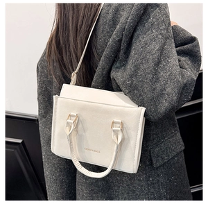 Dettaglio di borsa a mano bianca in pelle con tracolla indossata su cappotto grigio