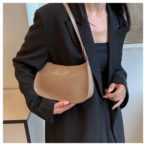 Side view of a light brown semi-circle underarm bag worn by a model in a black suit