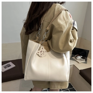 Detail of cream white leather tote bag with silver chain strap and tiger charm