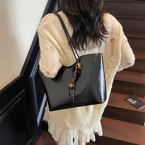 Fashionable black glossy faux leather tote bag with decorative metal bell keychain charm