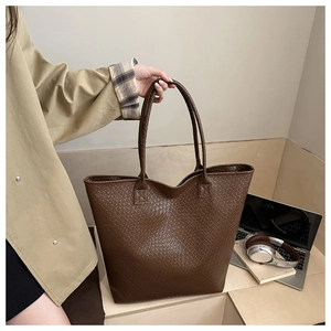Detailed view of dark brown woven tote bag next to a laptop in a casual office setting