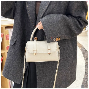 Detail view of a beige leather flap bag with dual gold buckles and chain strap