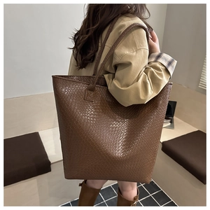 Deep brown tote bag with woven texture shown on shoulder for size reference