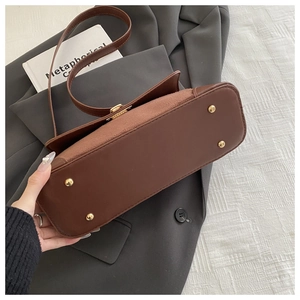 Detail view of the brown underarm bag showing metal feet and leather suede patchwork